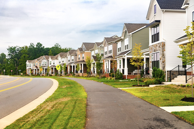 Quiet street in a residential area in the suburbs. Rows of houses along the sidewalk with a green lawn.